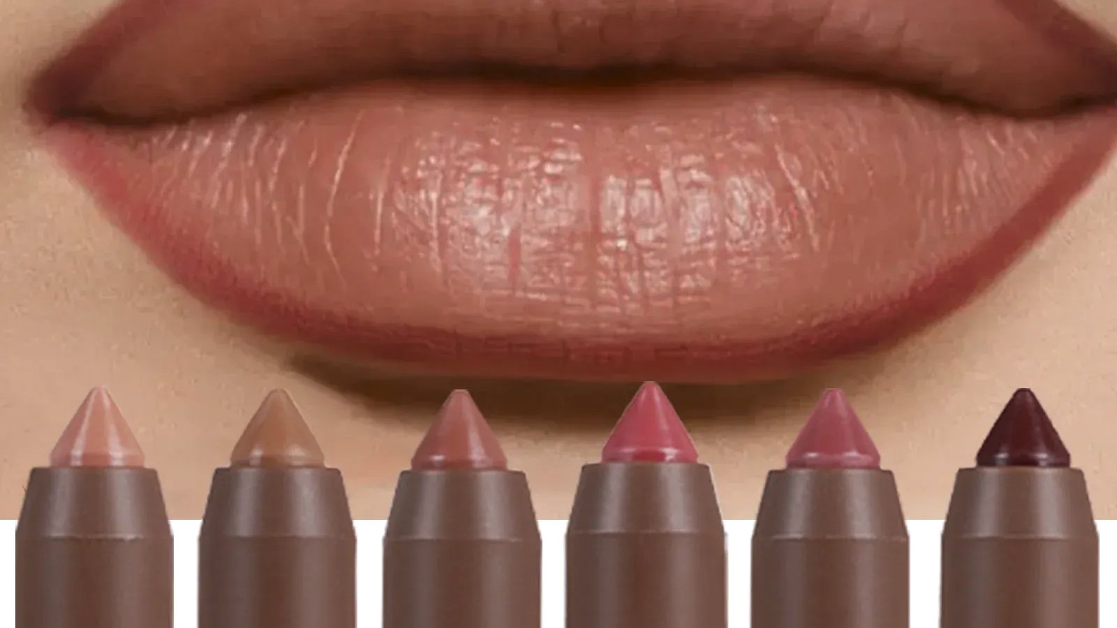 Soft nude and brown matte lip crayons and pencils arranged on marble beside a swatch of nude-pink colour